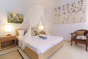 A bedroom with a bed, nightstands, a chair, and artwork on the walls. - a traditional old-style Balinese homestay in the centre of Ubud (Gianyar)