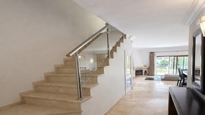 Un intérieur moderne avec un escalier en marbre, un téléviseur à écran plat et une vue sur l’extérieur.