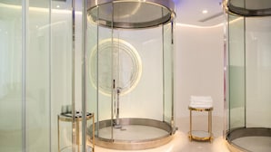Un ascenseur moderne, de forme circulaire, avec des parois en verre et une finition métallique, une petite table avec une serviette et un miroir rond.