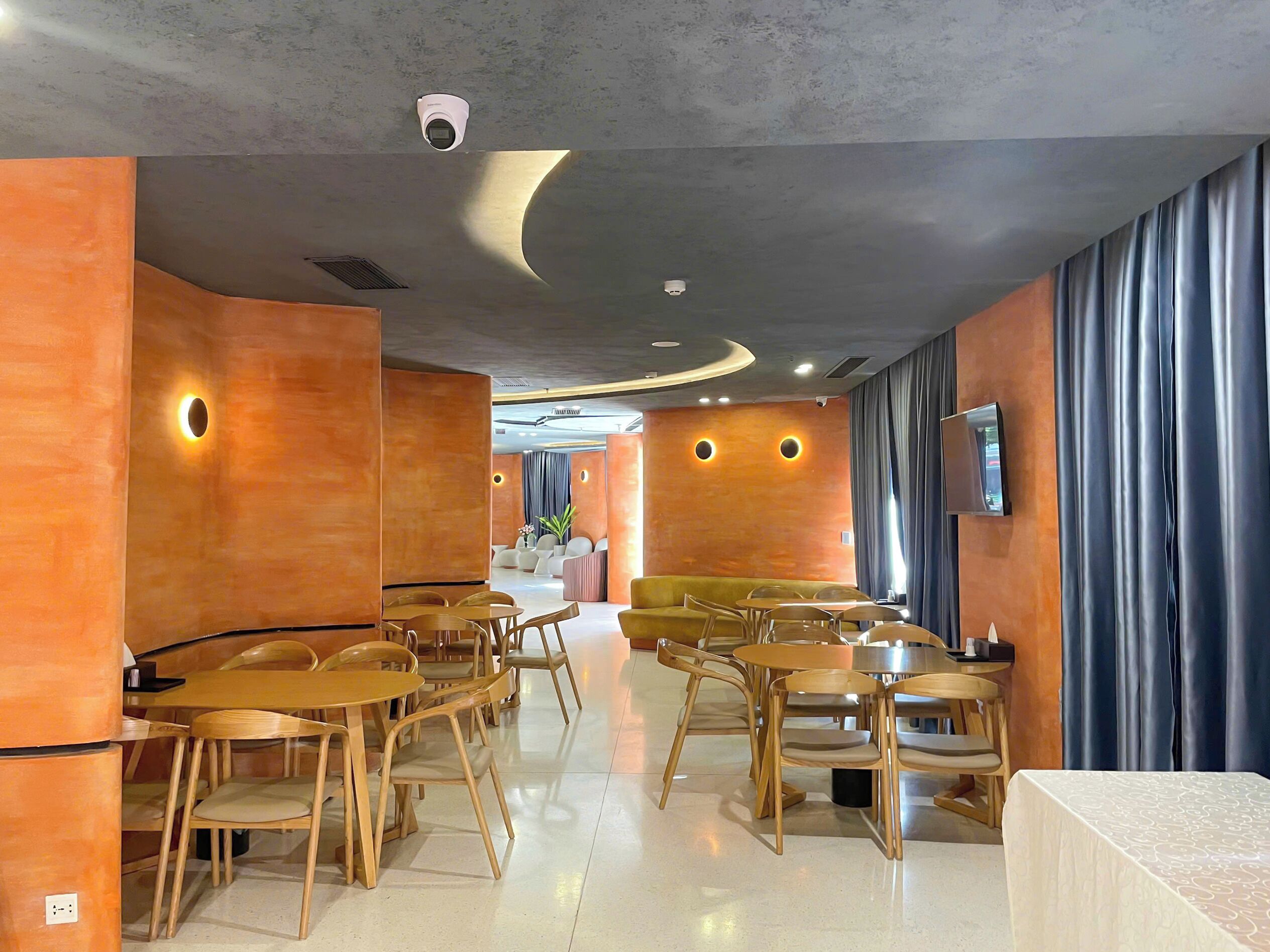 A modern interior with round tables and chairs, a sofa, and a TV mounted on the wall.