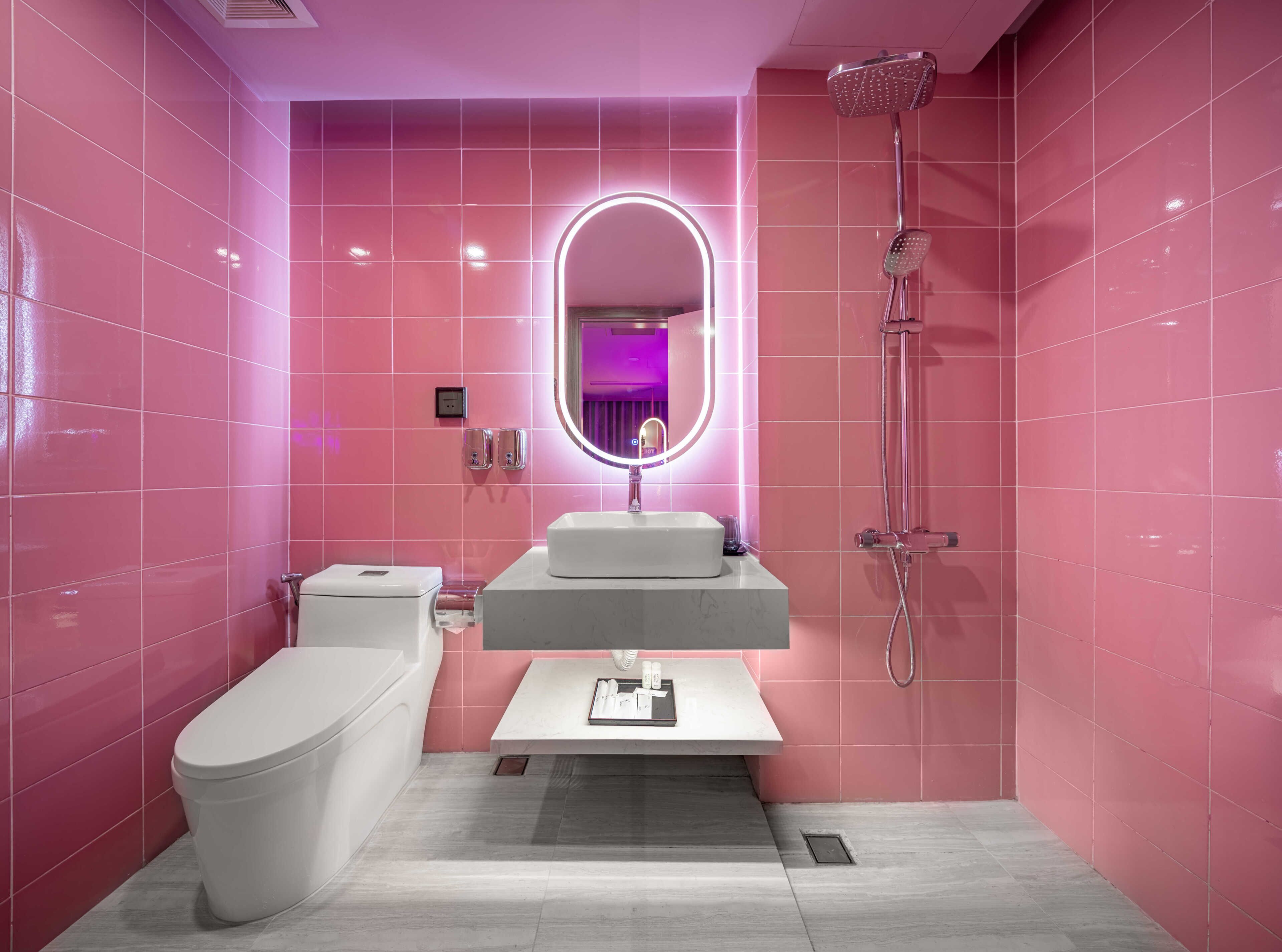 Ein modernes Badezimmer mit rosa gefliesten Wänden, einer weißen Toilette, einem Waschtisch mit Spiegel und einer Dusche.