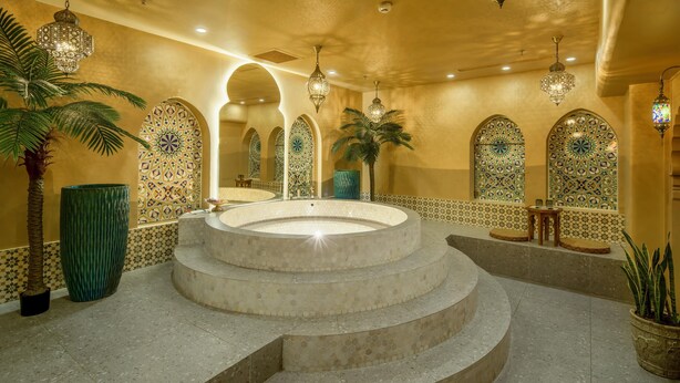 Un espace spa luxueux doté d’un jacuzzi circulaire, de murs recouverts de carreaux décoratifs et de lustres en cristal suspendus.