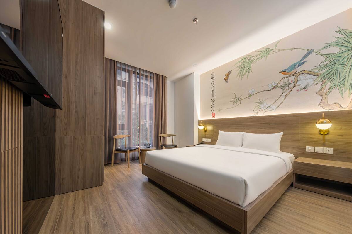 Une chambre d’hôtel moderne dotée d’un grand lit, d’un parquet, d’une œuvre d’art accrochée au mur et d’une fenêtre avec des rideaux.