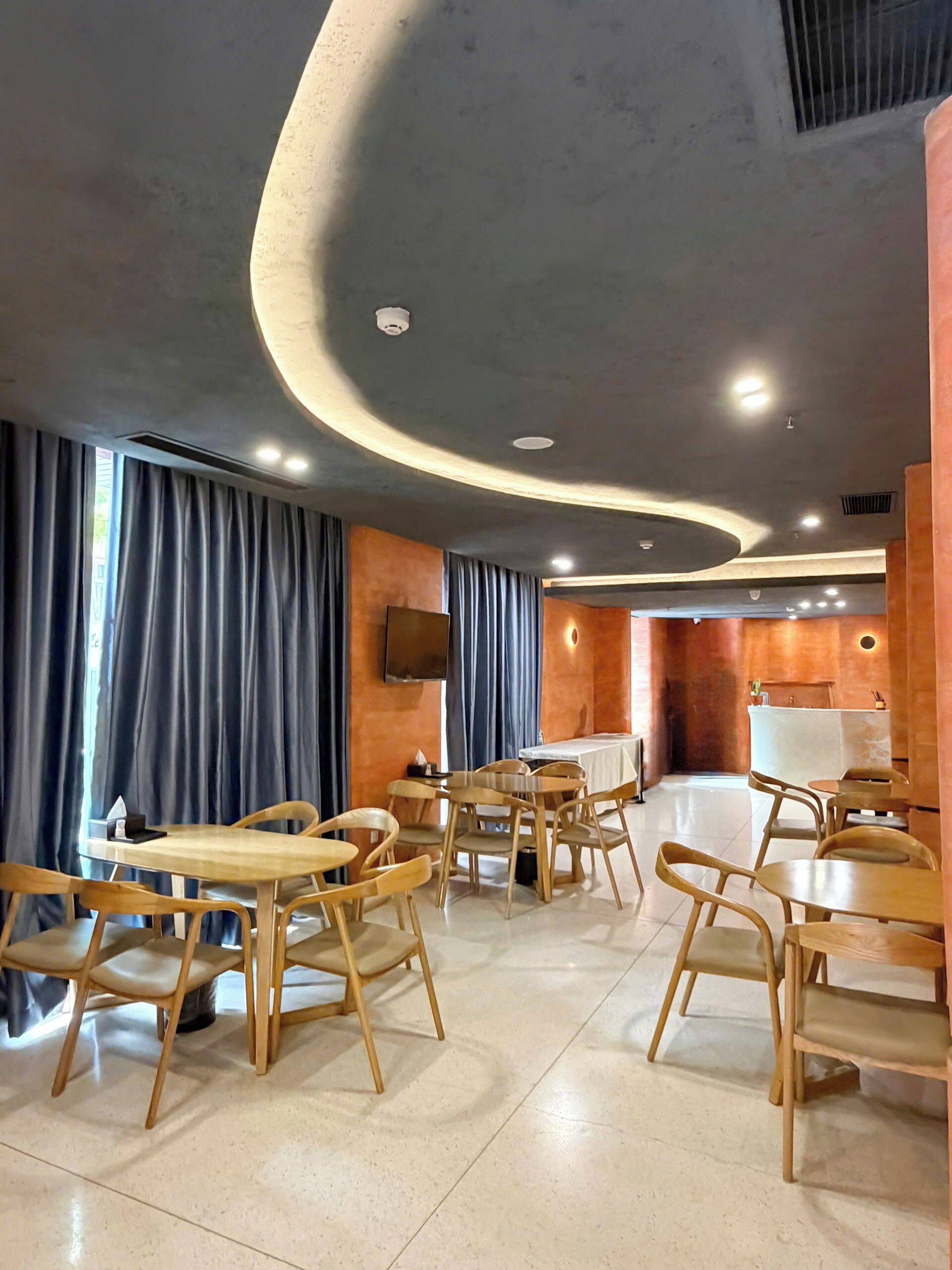 A modern interior with round tables and wooden chairs, a flat-screen TV mounted on the wall, and a counter area.