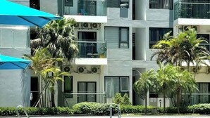 Un edificio moderno con varios balcones, piscina y vegetación circundante.