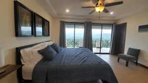 Ein Schlafzimmer mit Bett, Deckenventilator, Sessel und Balkon mit Blick.