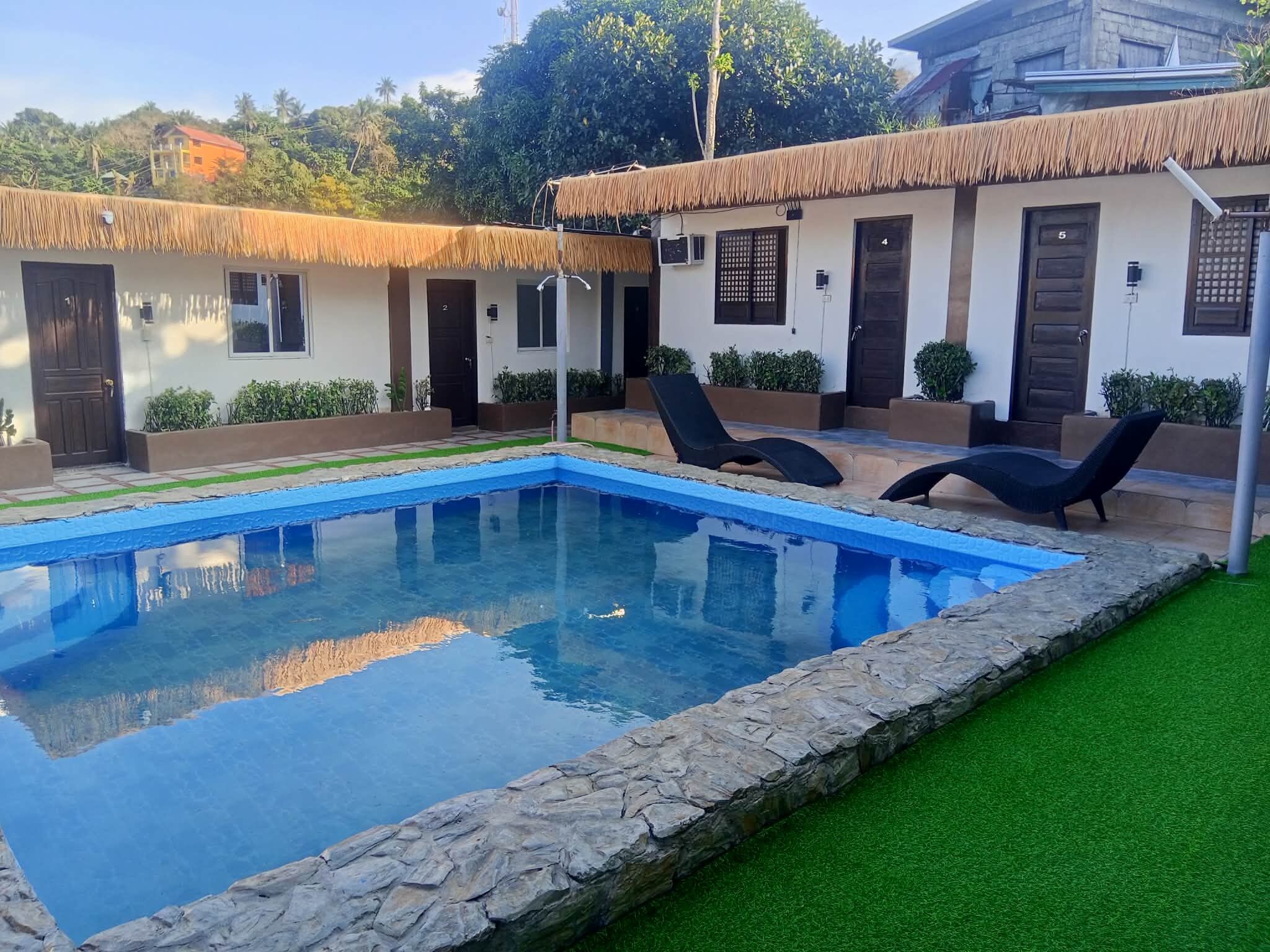 Una piscina con lettini, un bordo in pietra e un edificio con tetto di paglia.