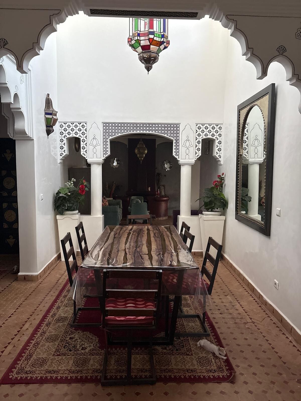 Un espace repas comprenant une table centrale, des chaises, un tapis à motifs et des éléments décoratifs tels qu’un miroir et des œuvres d’art mural.