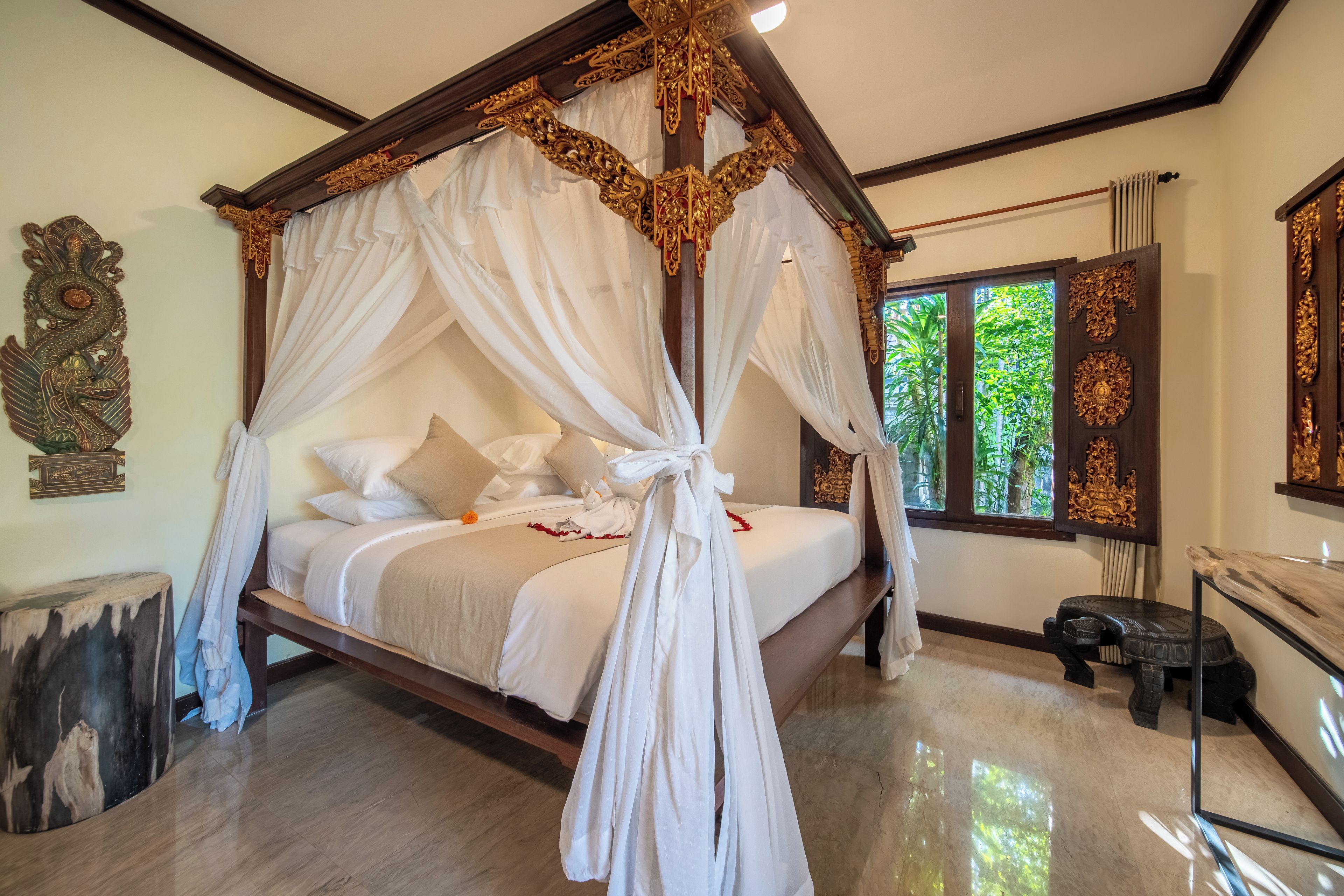 A four-poster bed with a canopy, a marble floor, and a view of greenery through the window.