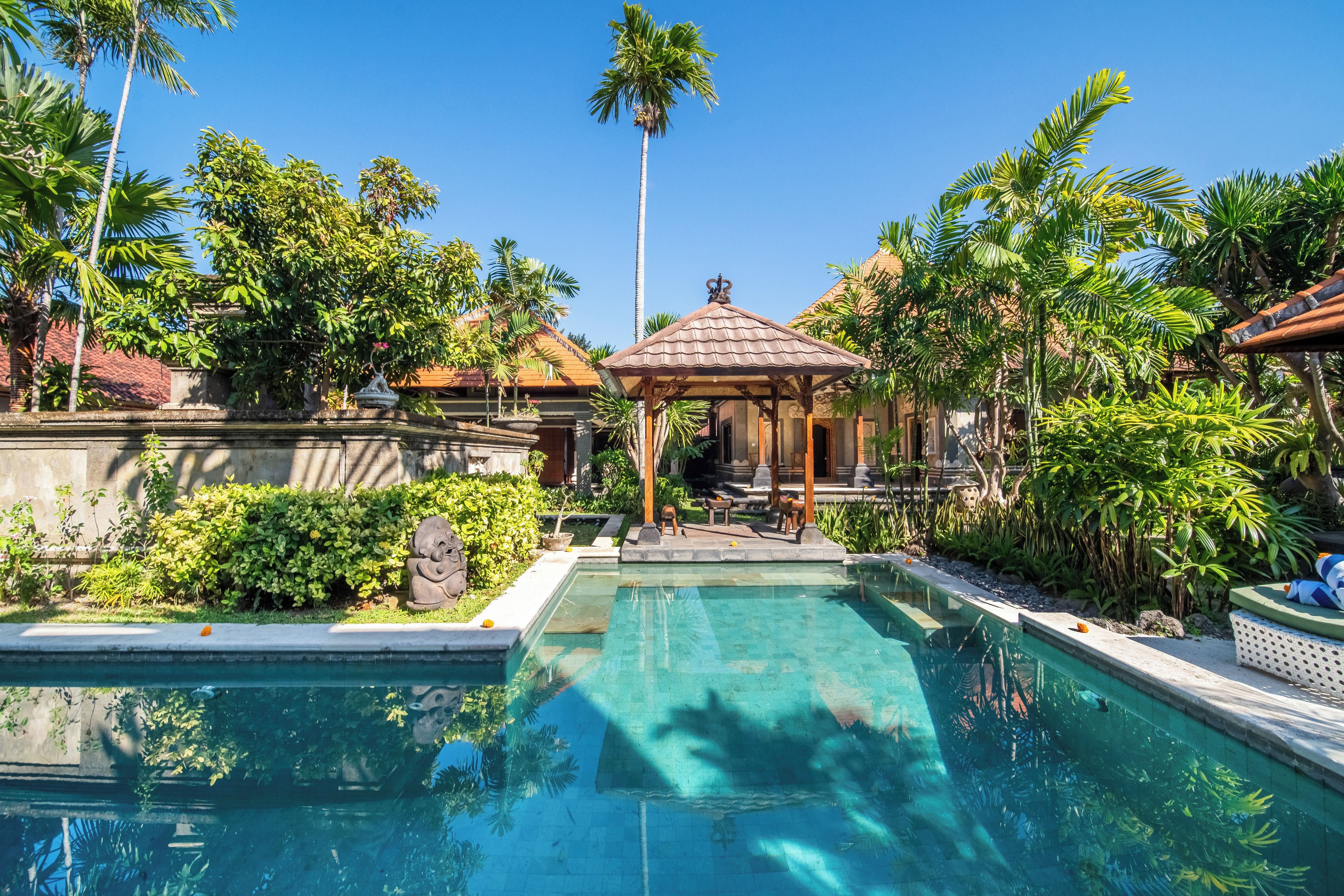 A swimming pool with a gazebo, surrounded by lush greenery and palm trees.