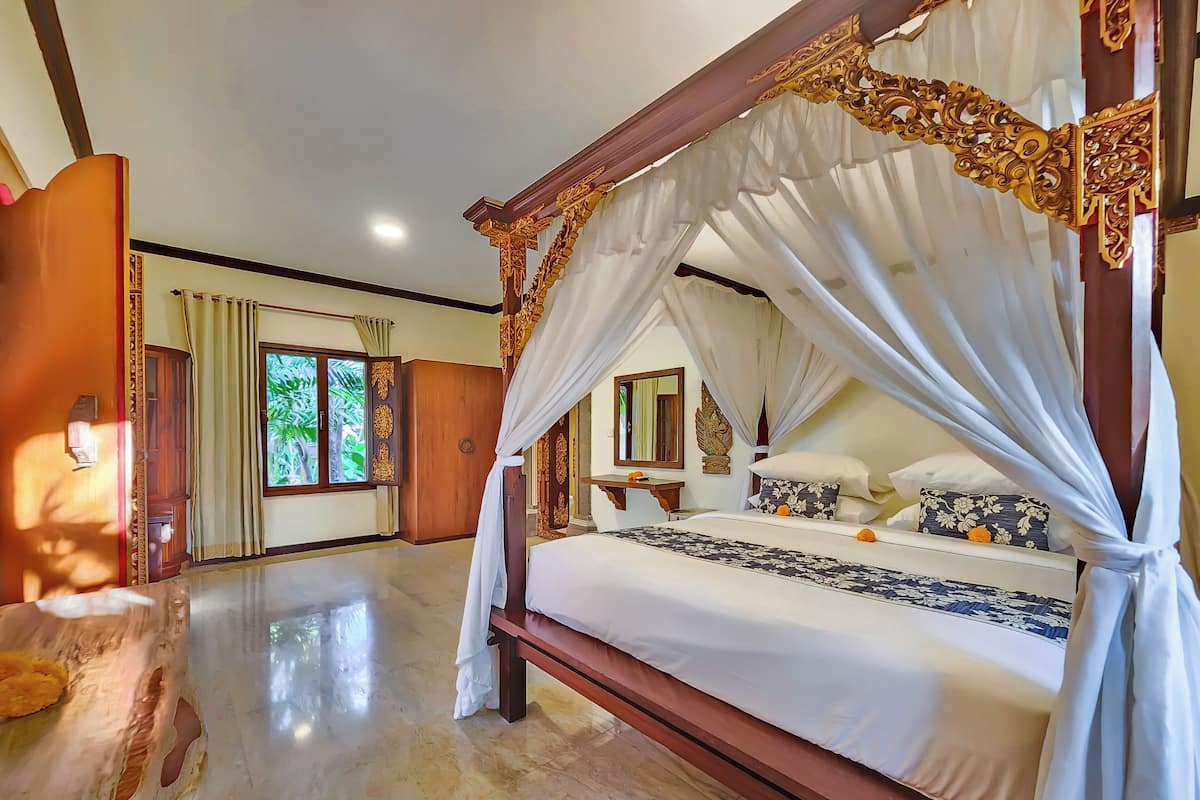 A spacious room with a large bed, a wooden wardrobe, and a window with curtains.