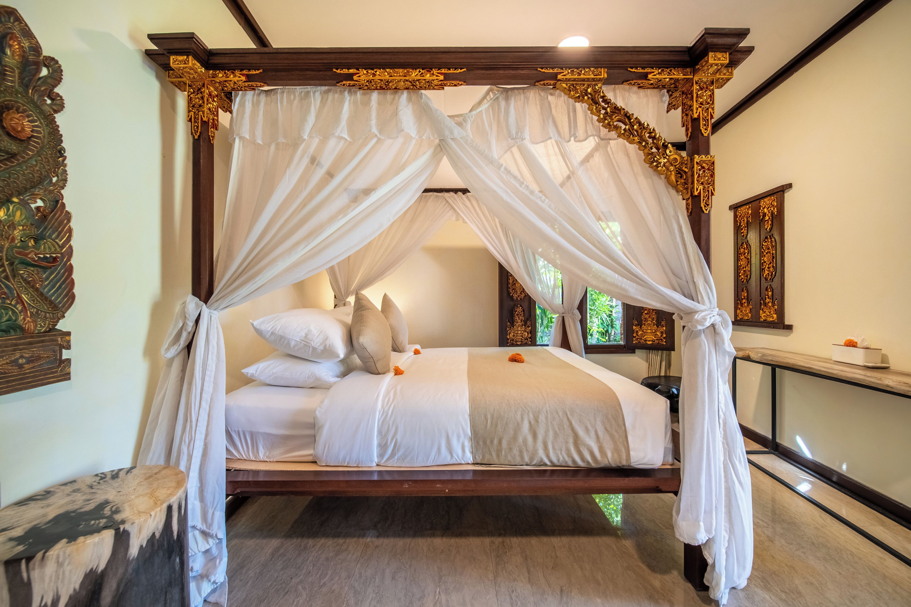 A four-poster canopy bed with white linens and a wooden frame, set in a room with traditional decor.