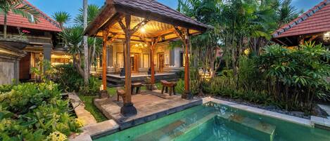 A poolside area with a gazebo, palm trees, and a clear pool.