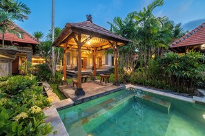 Un espace aménagé au bord de la piscine, avec un kiosque, des palmiers et une eau cristalline.