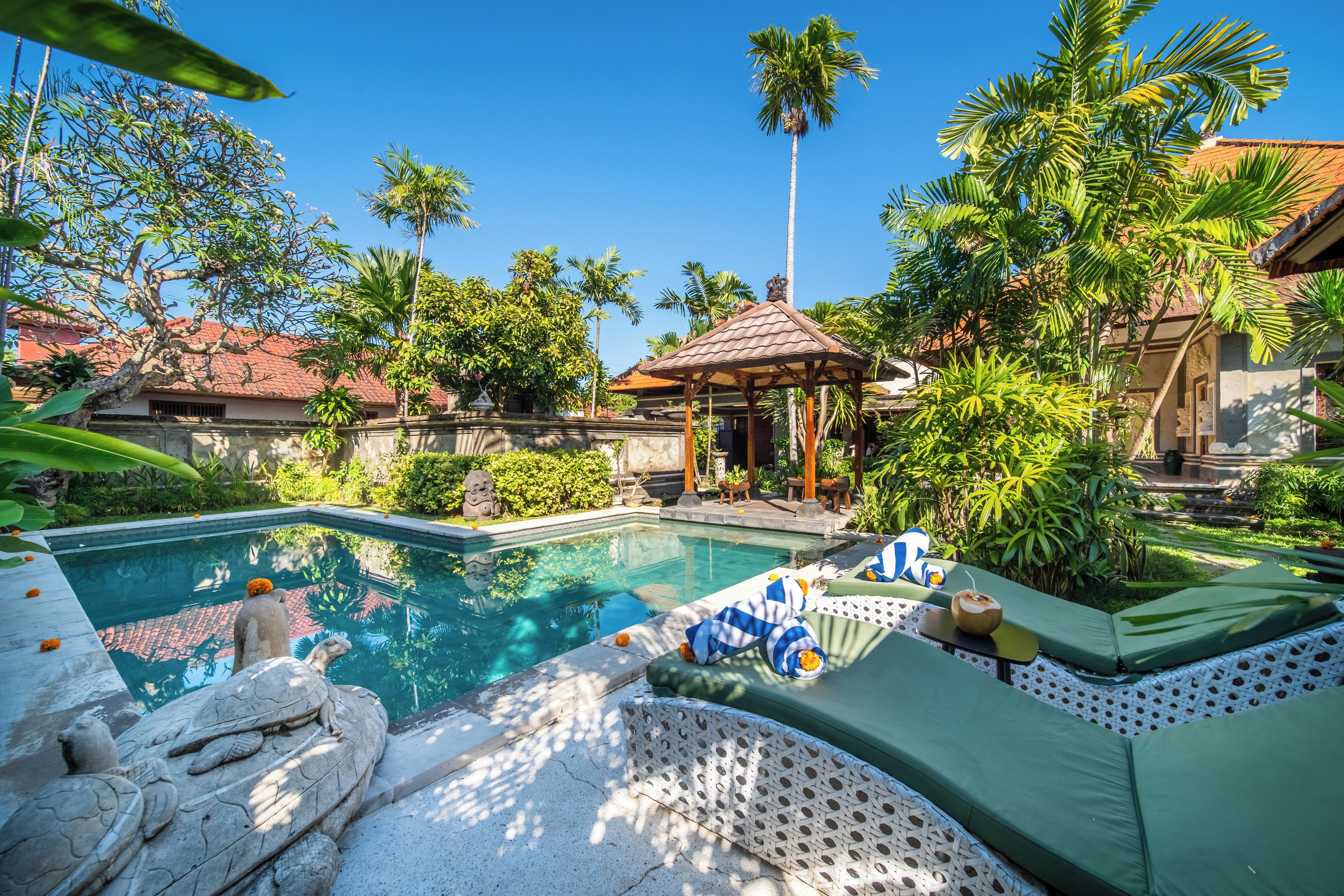 Un área de piscina con sillones de descanso, un pabellón y plantas tropicales.