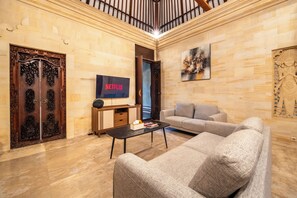 A living room with a sofa, a coffee table, a TV, and a wooden door with intricate carvings. - Villa Hibiscus Sanur by Nagisa Bali (Denpasar)
