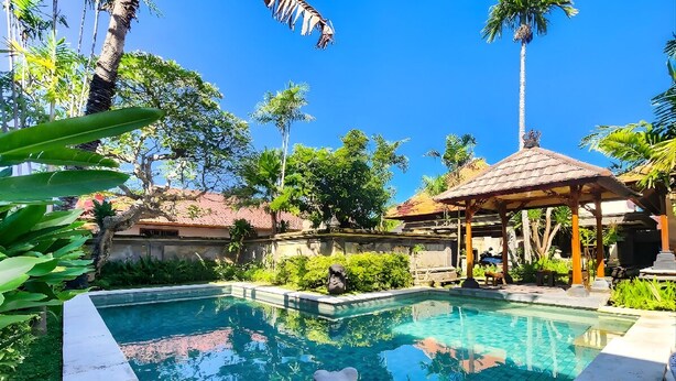 A swimming pool with a bear statue, surrounded by palm trees and a gazebo. - Villa Hibiscus Sanur by Nagisa Bali (Denpasar)