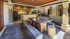 A spacious kitchen with a central island, wooden benches, and a stone floor. - Villa Hibiscus Sanur by Nagisa Bali (Denpasar)