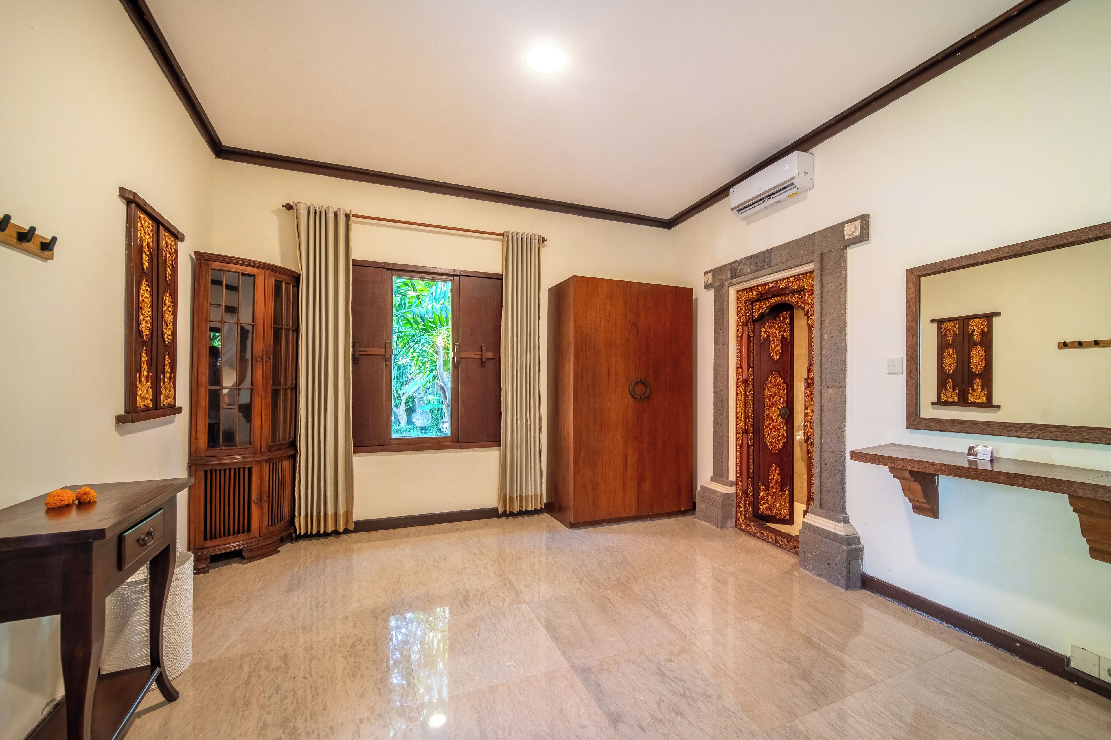 A room with a large window, a wooden wardrobe, a mirror, and a small table.