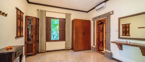 A room with a large window, a wooden wardrobe, a mirror, and a small table.
