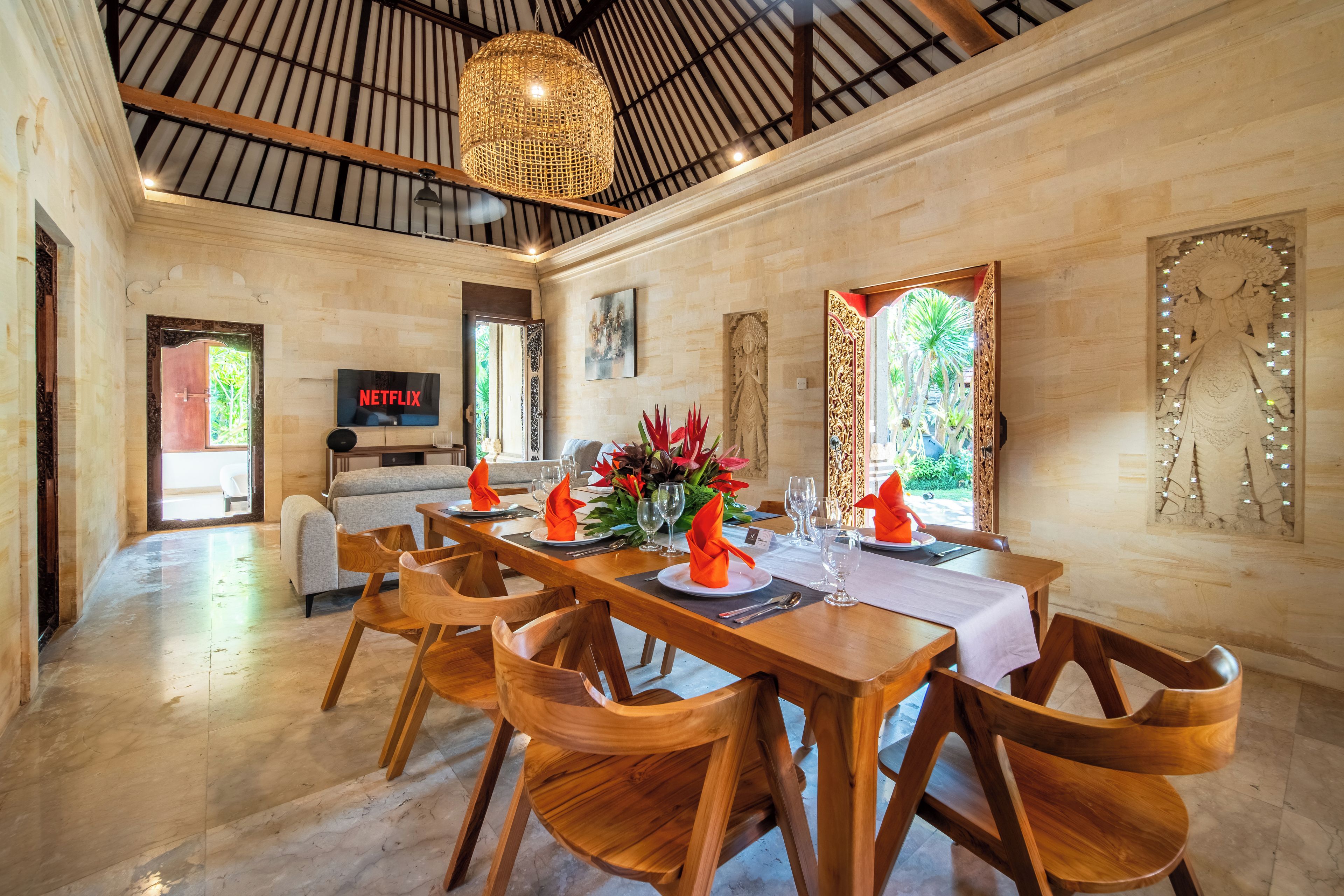 A dining area with wooden tables and chairs, a television displaying 'NETFLIX', and a ceiling with a woven light fixture.