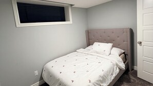 A bedroom with a bed, a window, a door, and a ceiling light.
