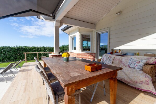 An outdoor patio with a wooden table, wicker chairs, a sofa, and a potted plant.