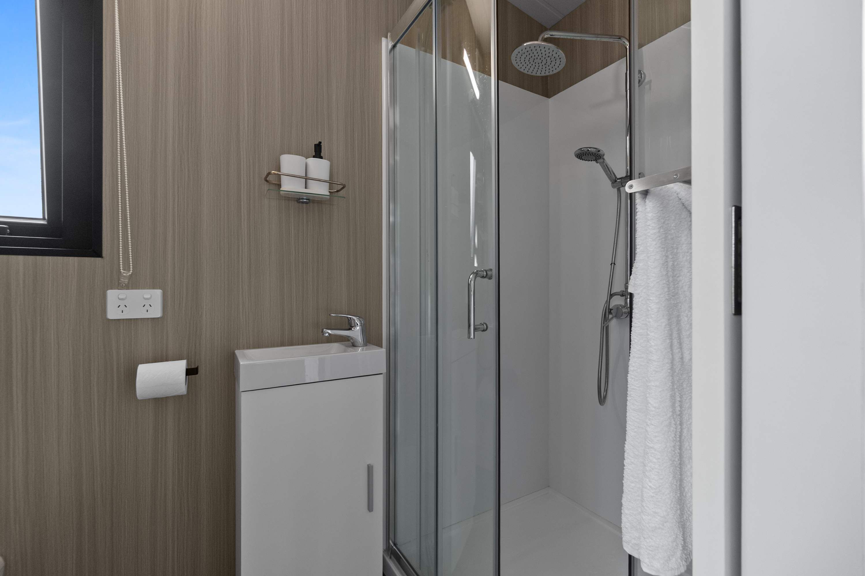 A modern bathroom with a glass shower enclosure, a sink with a mirror, and a towel rack.