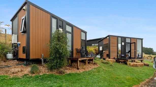 Two modern, wooden cabins with large windows, outdoor seating, and a clear sky.