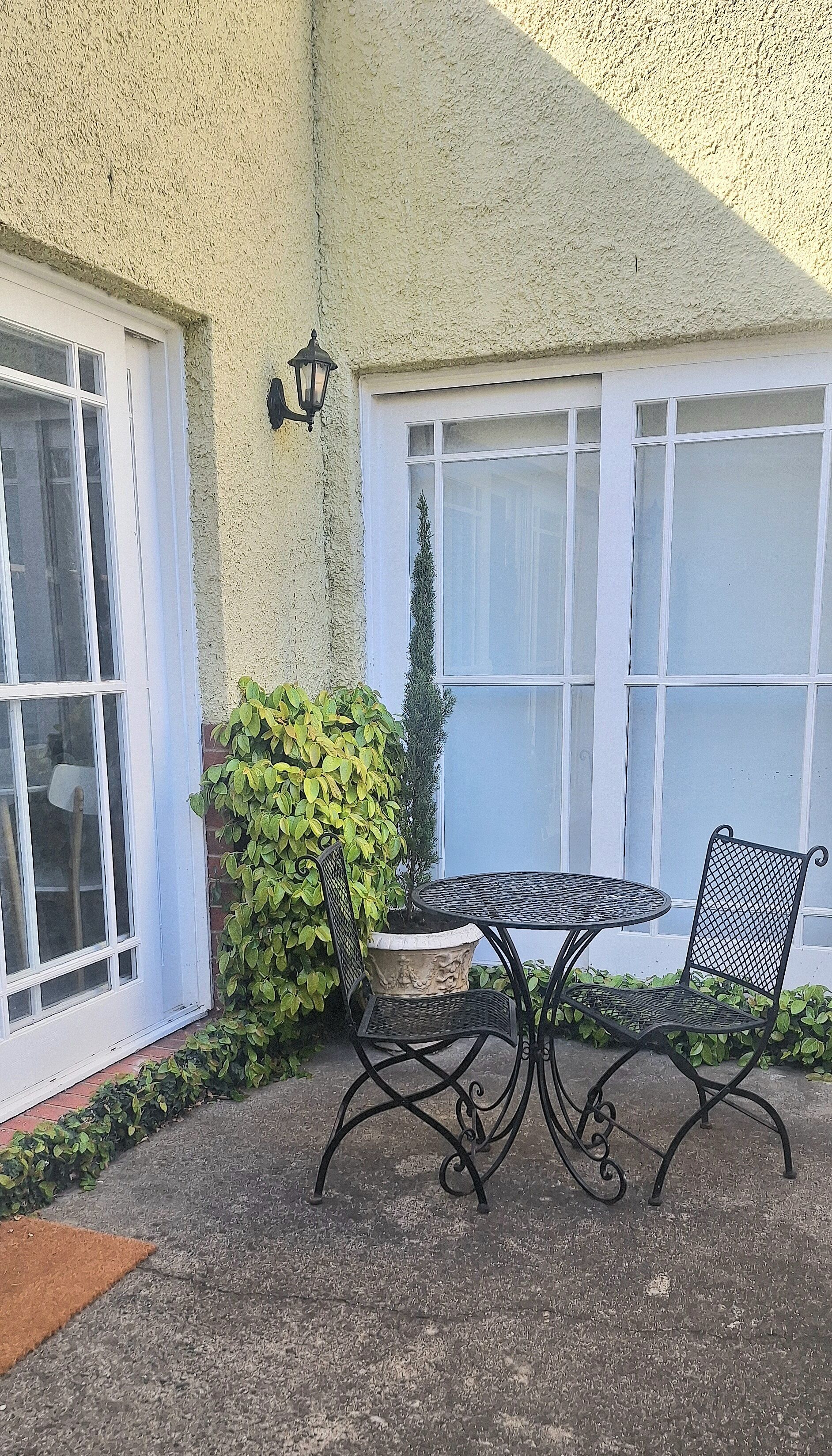A patio with a round table and two chairs, a potted plant, and a wall-mounted light fixture.