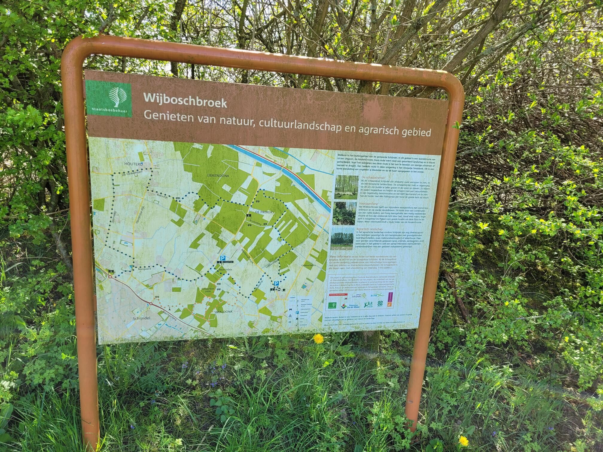 A signboard with a map and text, surrounded by greenery.
