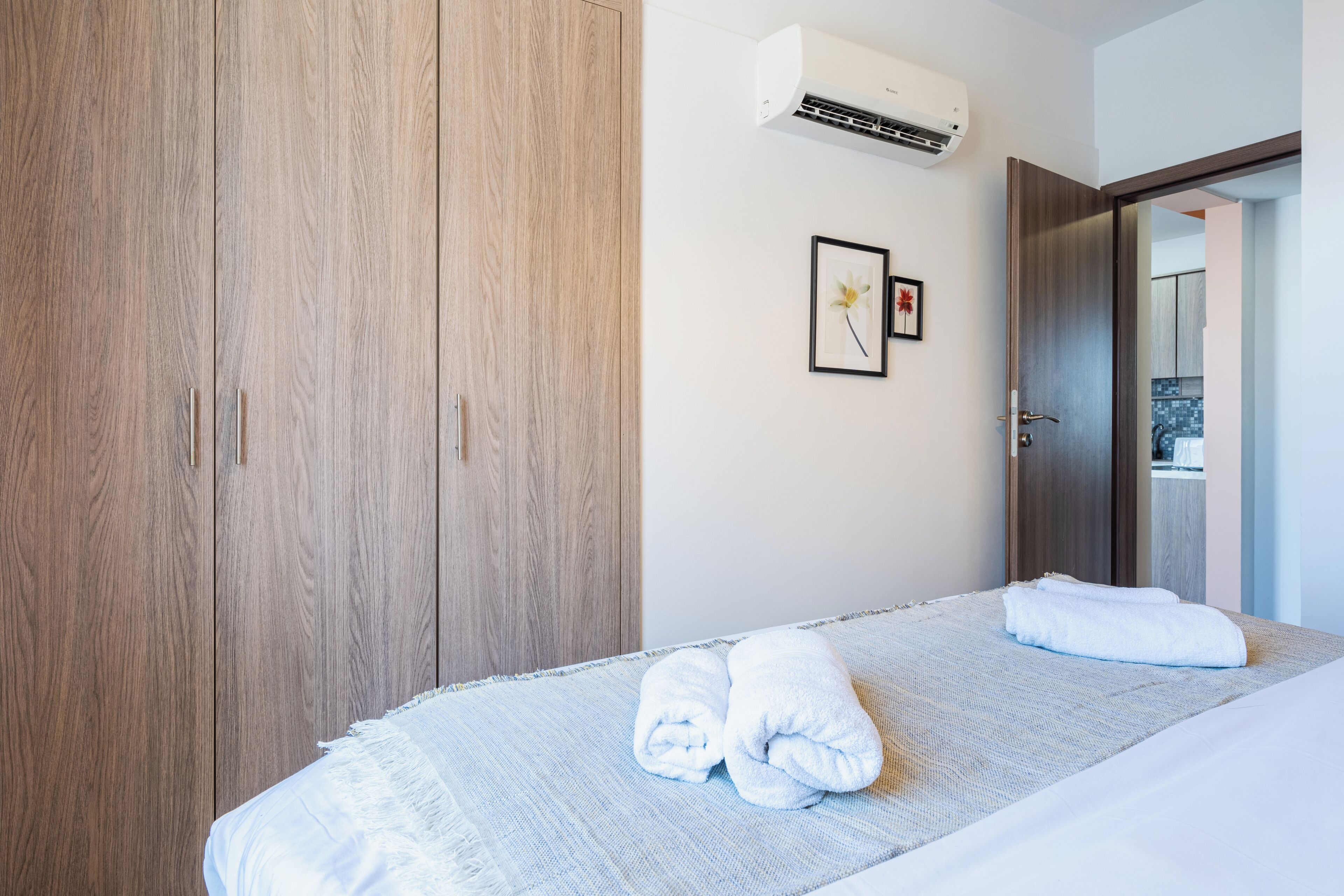 A hotel room with a bed, a wooden wardrobe, an air conditioning unit, and a framed picture on the wall.