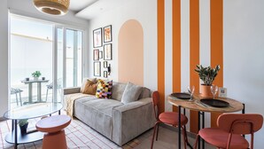 En moderne stue med sofa, spisebord, stole, en hængende lampe og et stort vindue.