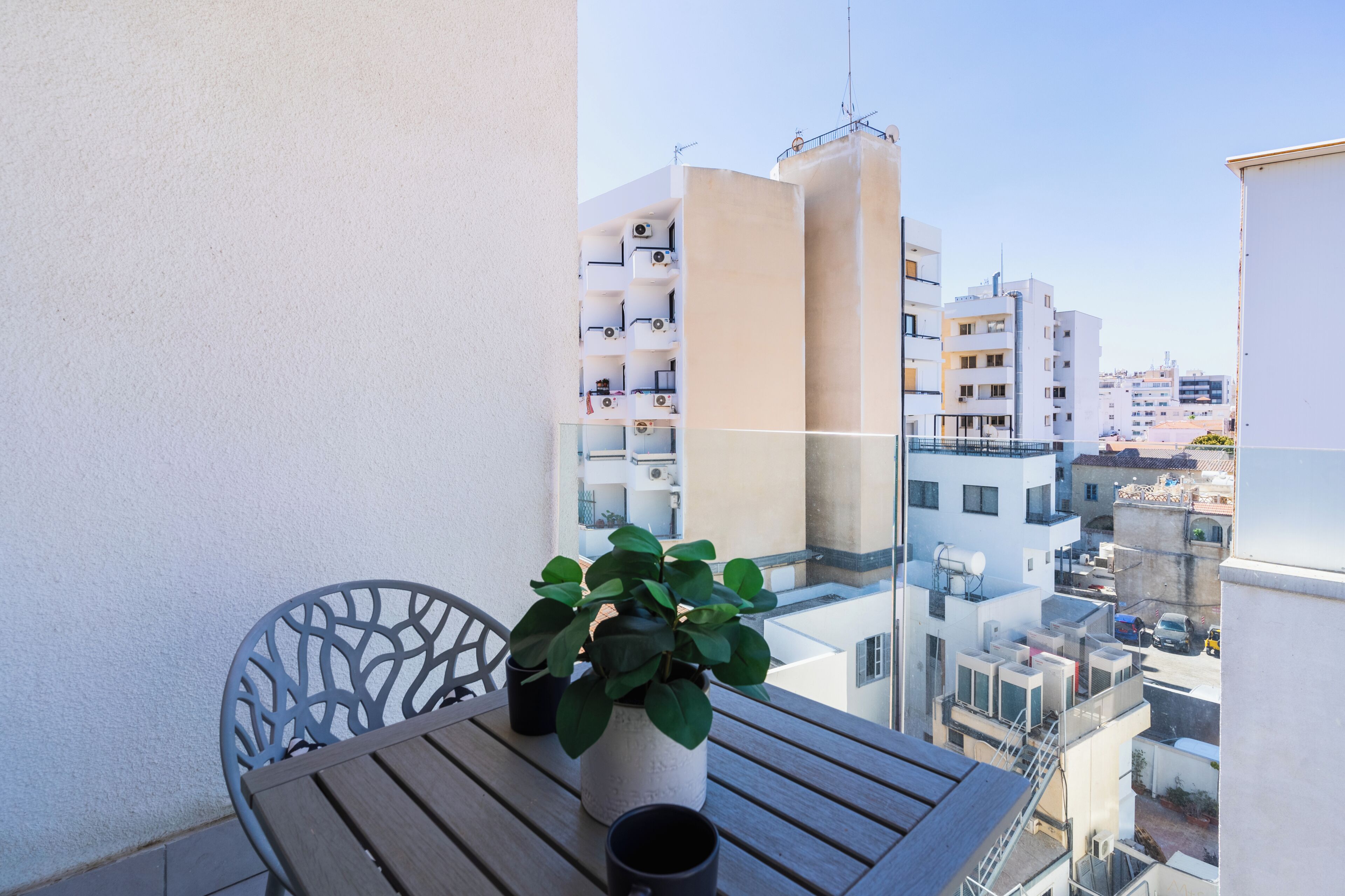 A balcony with a table, chairs, a potted plant, and a view of surrounding buildings.