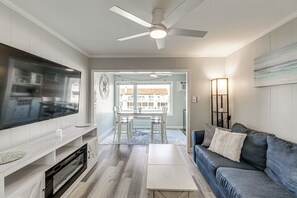A modern living room with a flat-screen TV, a ceiling fan, a dining area with a table and chairs, and a sofa with cushions. - Bayside Waterfront Retreat in Ocean City! (Ocean City)