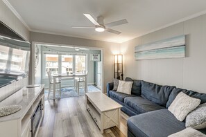 Een moderne woonkamer met een bank, een salontafel, een plafondventilator en een eethoek met een tafel en stoelen.