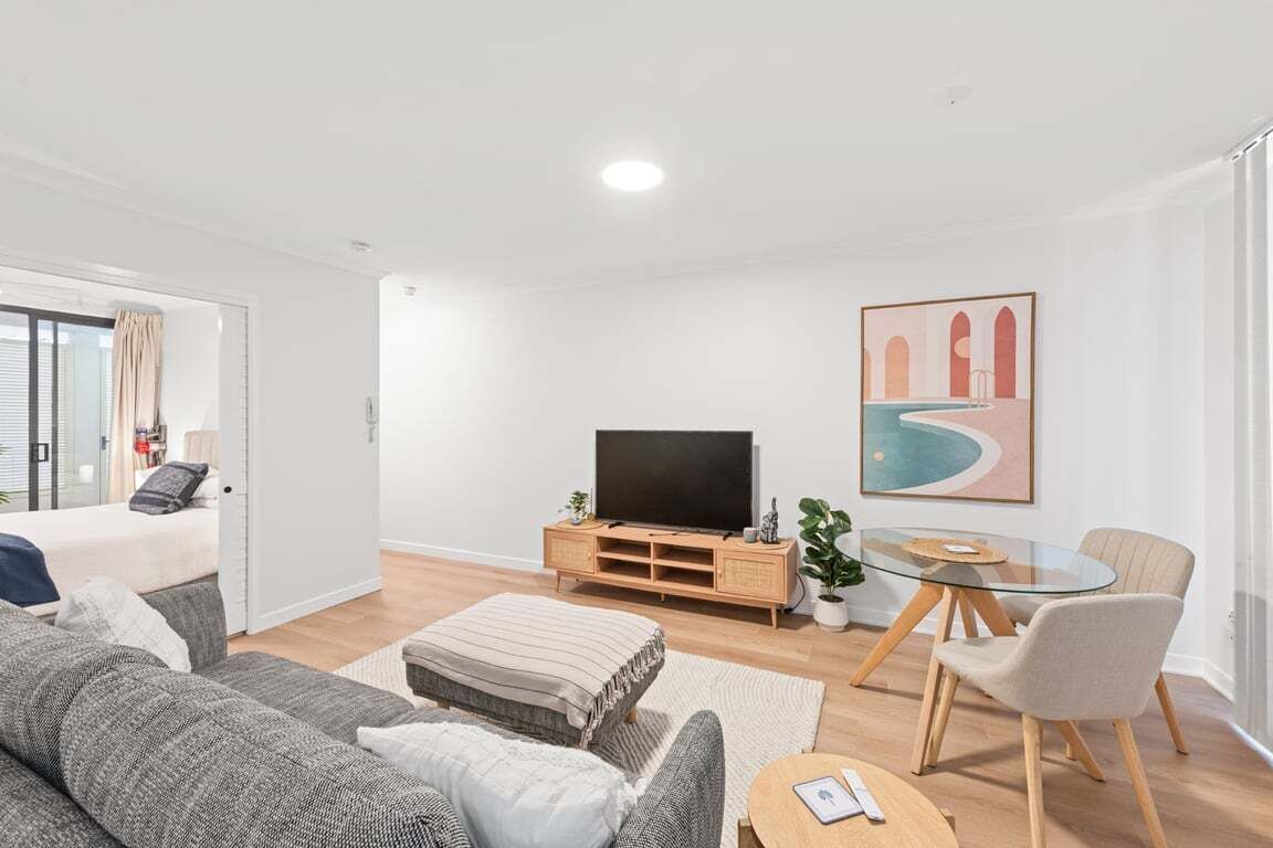 A modern living room with a sofa, a glass coffee table, a TV on a wooden stand, and a painting on the wall.