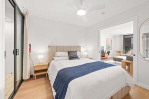 Ein Schlafzimmer mit einem Bett, Nachttischen, einem Deckenventilator und Blick auf einen anderen Raum.