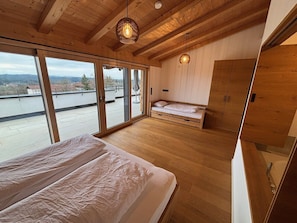 Ein Schlafzimmer mit einem großen Bett, einem kleineren Bett, einem Kleiderschrank und Blick ins Freie durch große Fenster.