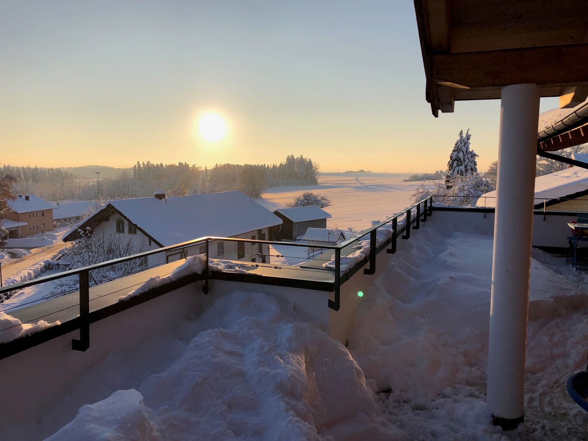Lumipeitteinen maisema, jossa on rakennuksia, kaide ja kirkas taivas.