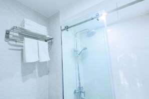 Une douche fermée par des parois en verre, dotée d’un pommeau de douche à main et d’un porte-serviettes mural avec des serviettes pliées.