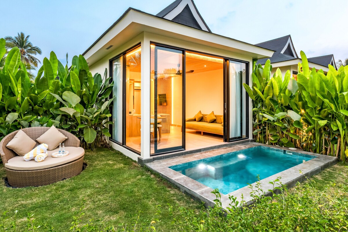 Una casa moderna con un salón acristalado, piscina y abundante vegetación.