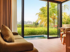 Una sala de estar moderna con un sofá, un comedor con sillas y vistas a una piscina y abundante vegetación.