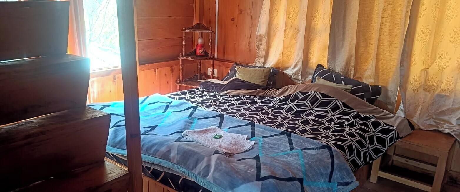 A wooden room with a bed, a nightstand, and a small wooden stool.