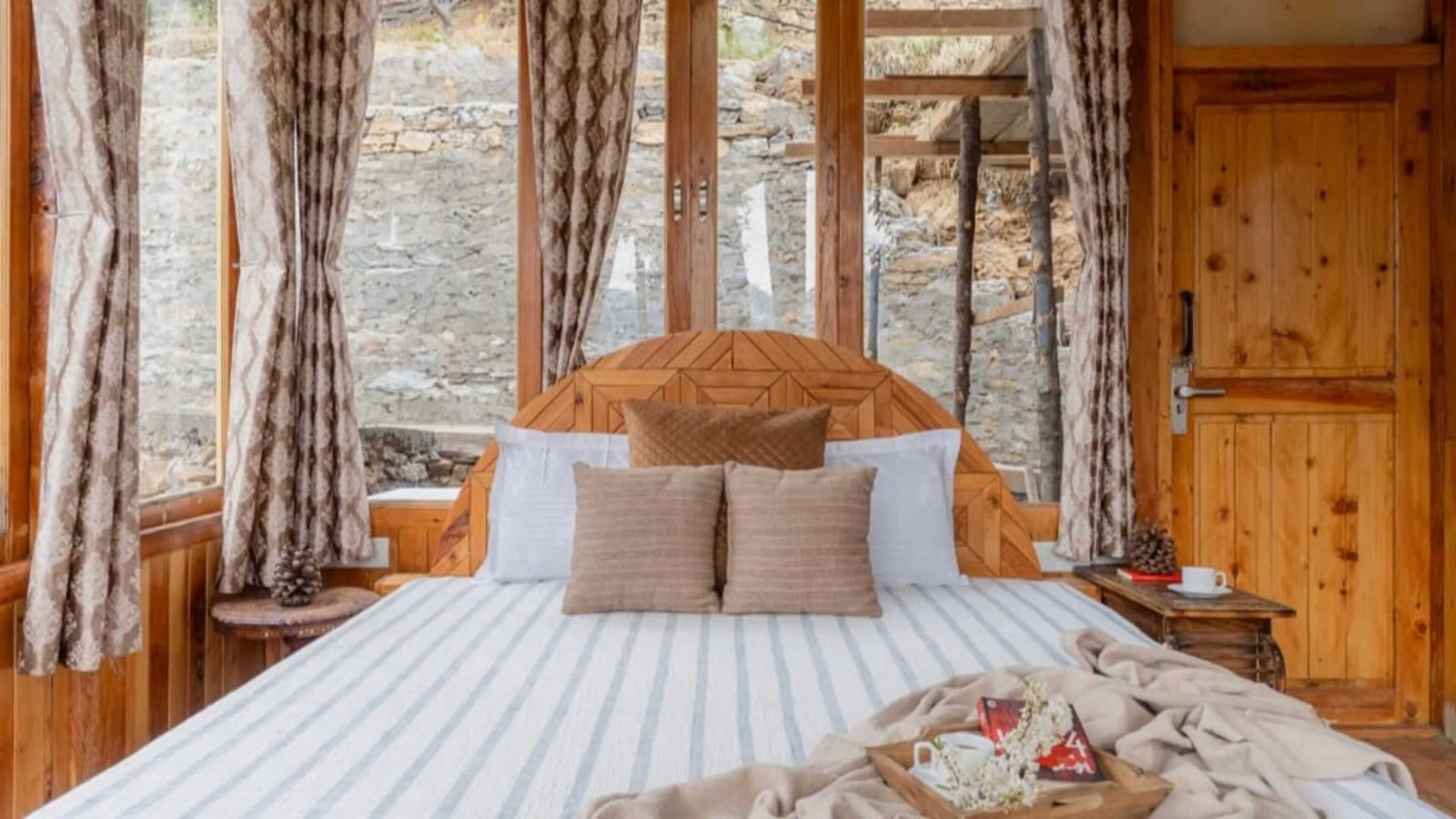 A bed with a wooden headboard, striped bedding, and a tray with a mug and flowers.