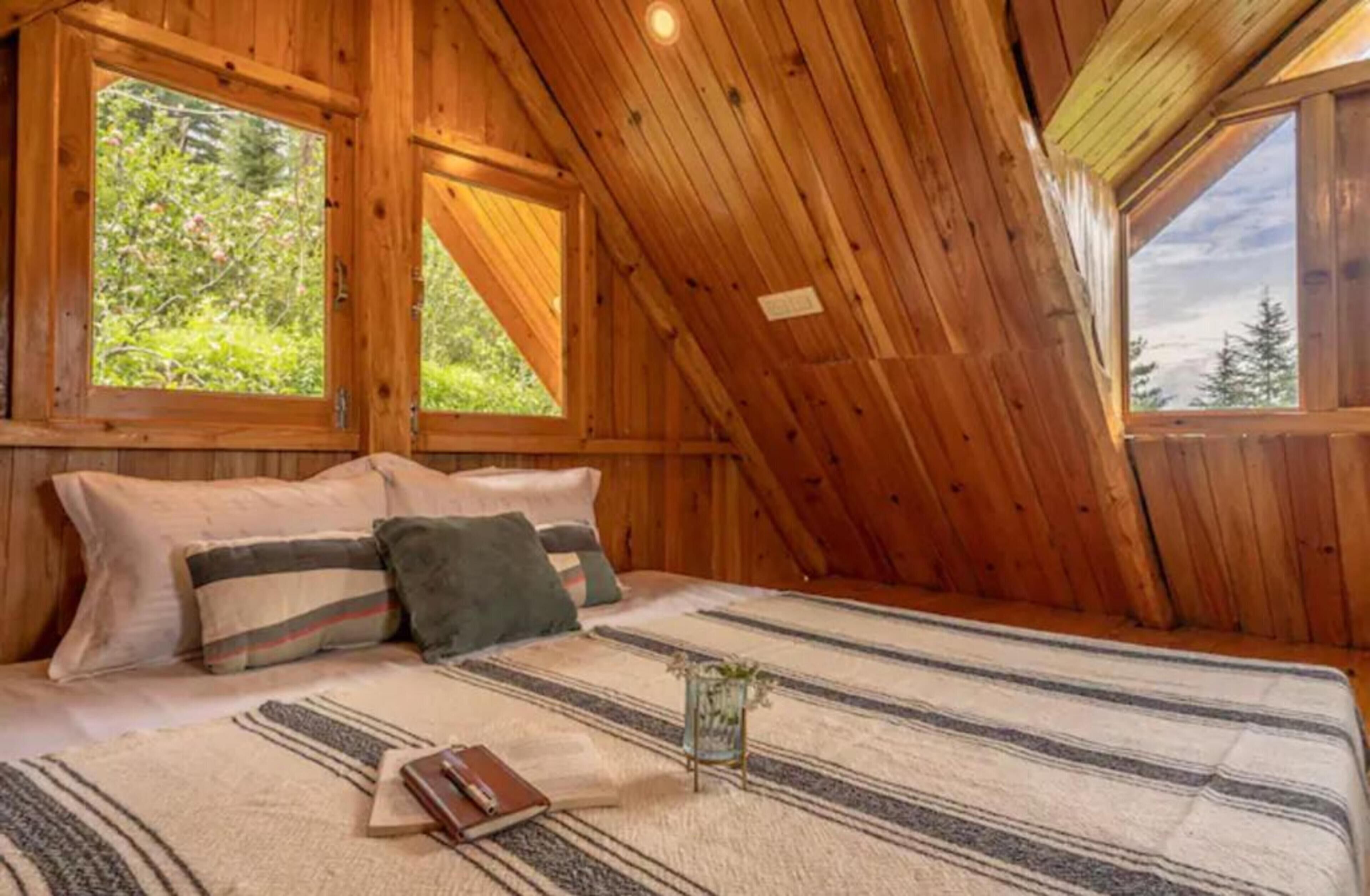 Une pièce en bois avec un plafond en pente, un lit avec des oreillers, une table de chevet et une fenêtre.