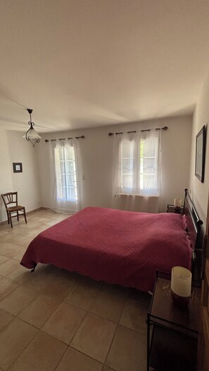 A bedroom with a large bed, two windows with curtains, a chair, a bedside table with a lamp, and a ceiling fan. - Gite for 4 people in the countryside each room has its own bathroom and private wc (Visan)