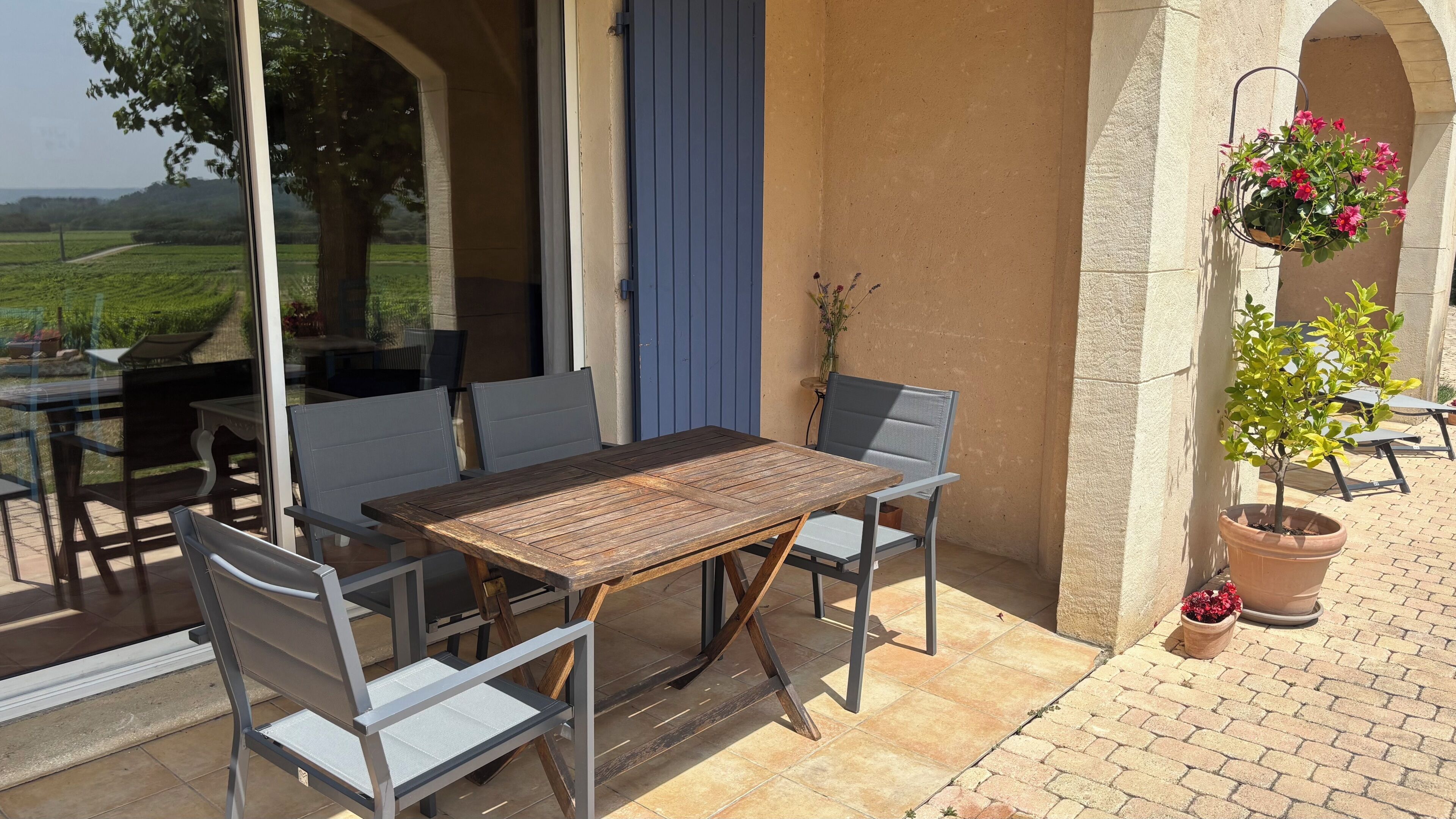 Une terrasse extérieure avec une table et des chaises, une jardinière suspendue et des plantes en pot.