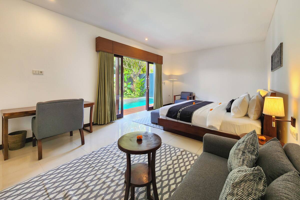 Ein Hotelzimmer mit Bett, Sofa, Schreibtisch, Stuhl und Blick auf einen Swimmingpool.