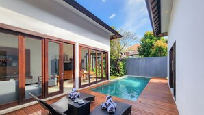 A modern outdoor pool area with wooden decking, lounge chairs, and a dining set. - Villa Movida Canggu by Nagisa Bali (Kerobokan)